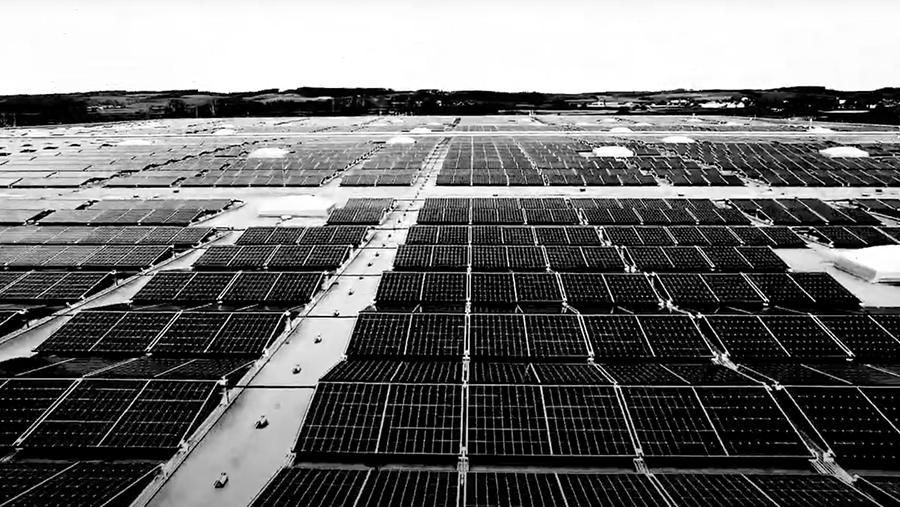 Black and white image depicting a vast array of solar panels installed on a large, flat surface with distant hills visible in the background.