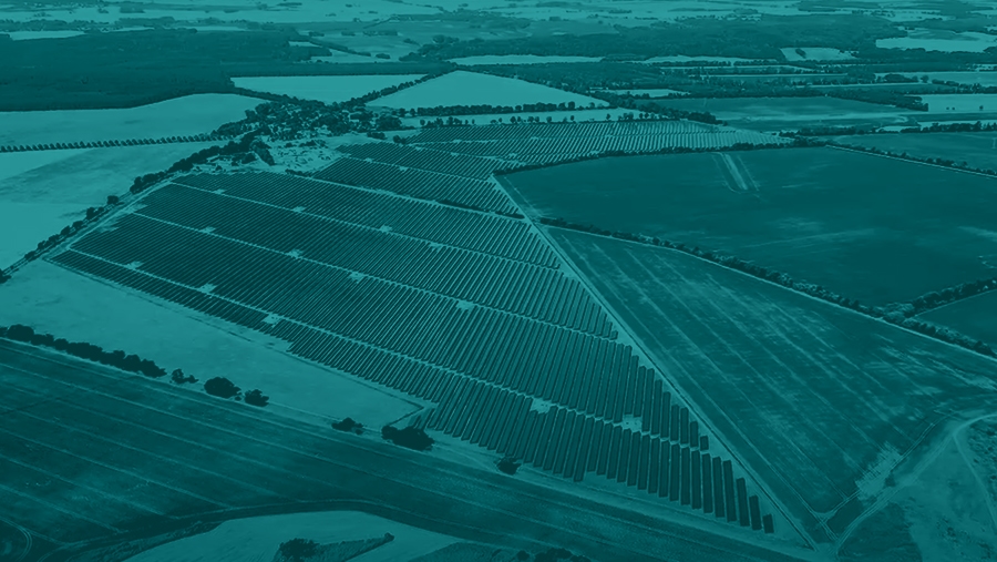 Aerial view of a large solar farm with many rows of solar panels installed in a rural landscape. Fields and farmlands surround the installation.