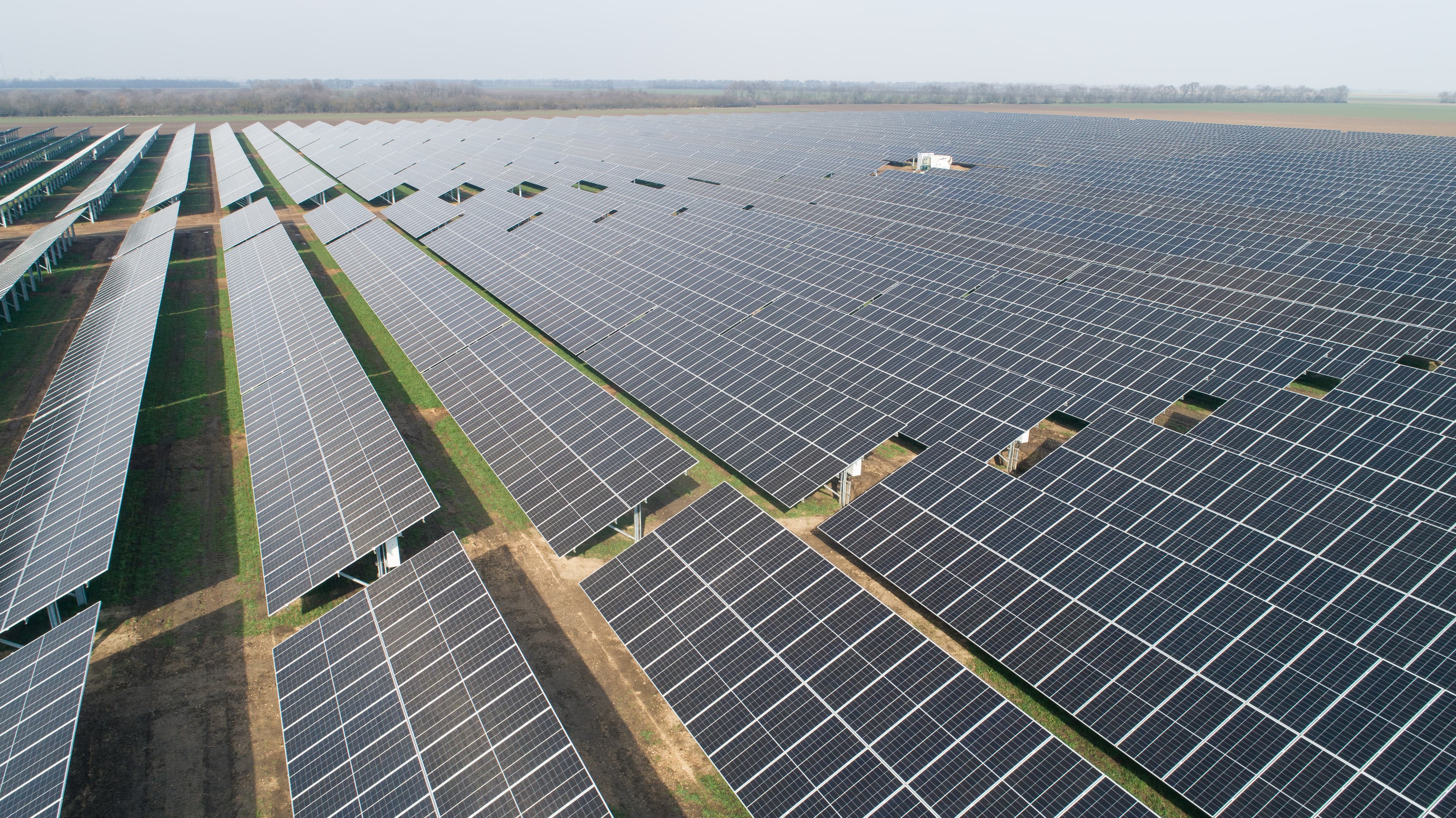 Aerial view of a large solar farm with rows of solar panels extending to the horizon under a clear sky.