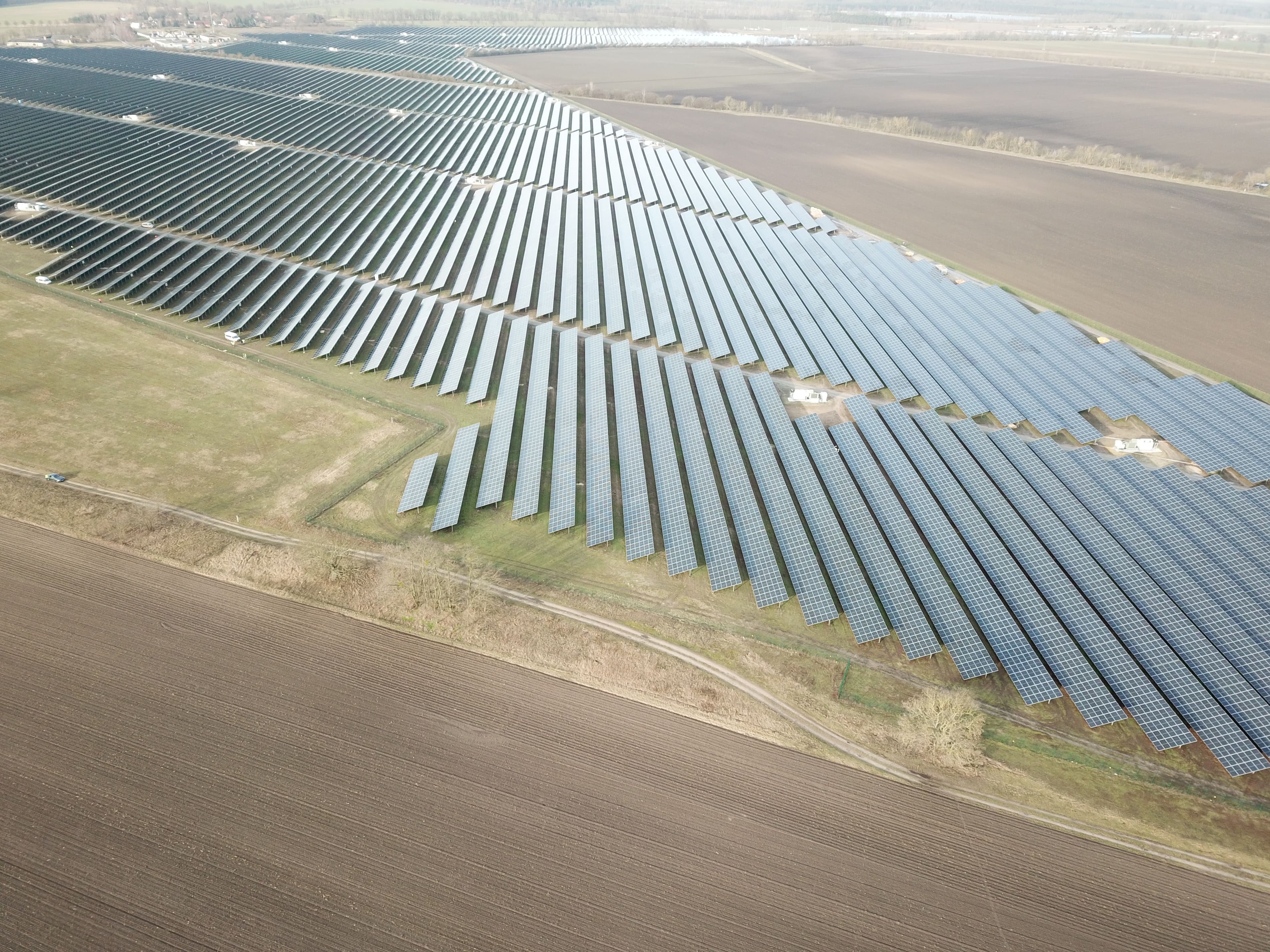 Aerial view of an extensive solar panel farm covering large sections of land in a rural area with fields surrounding it.