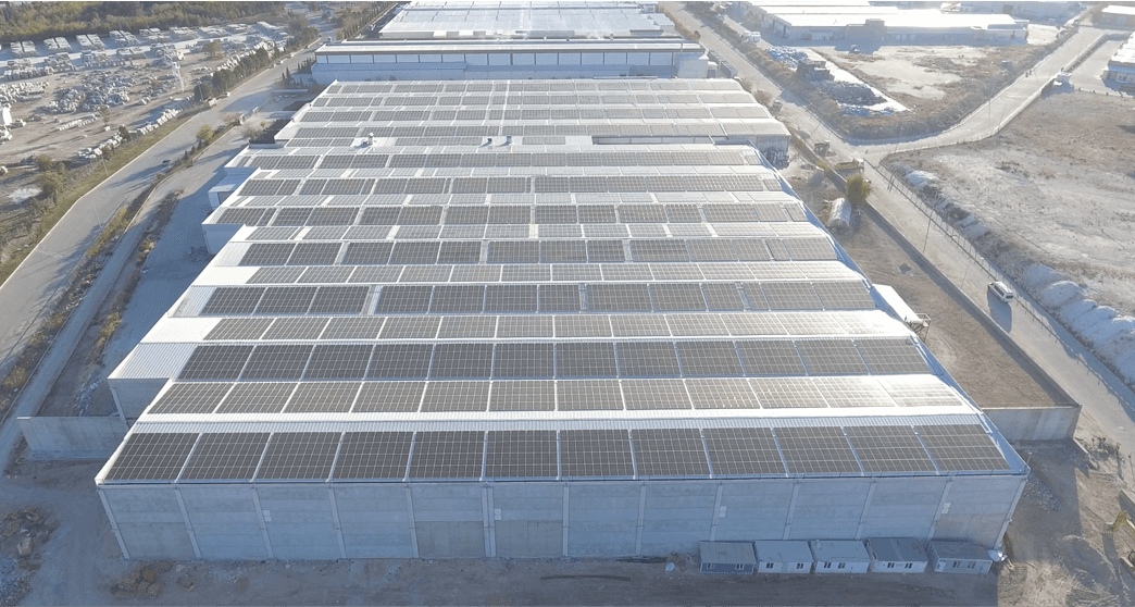 Aerial view of large industrial warehouses with rows of solar panels on the rooftops in a commercial area.