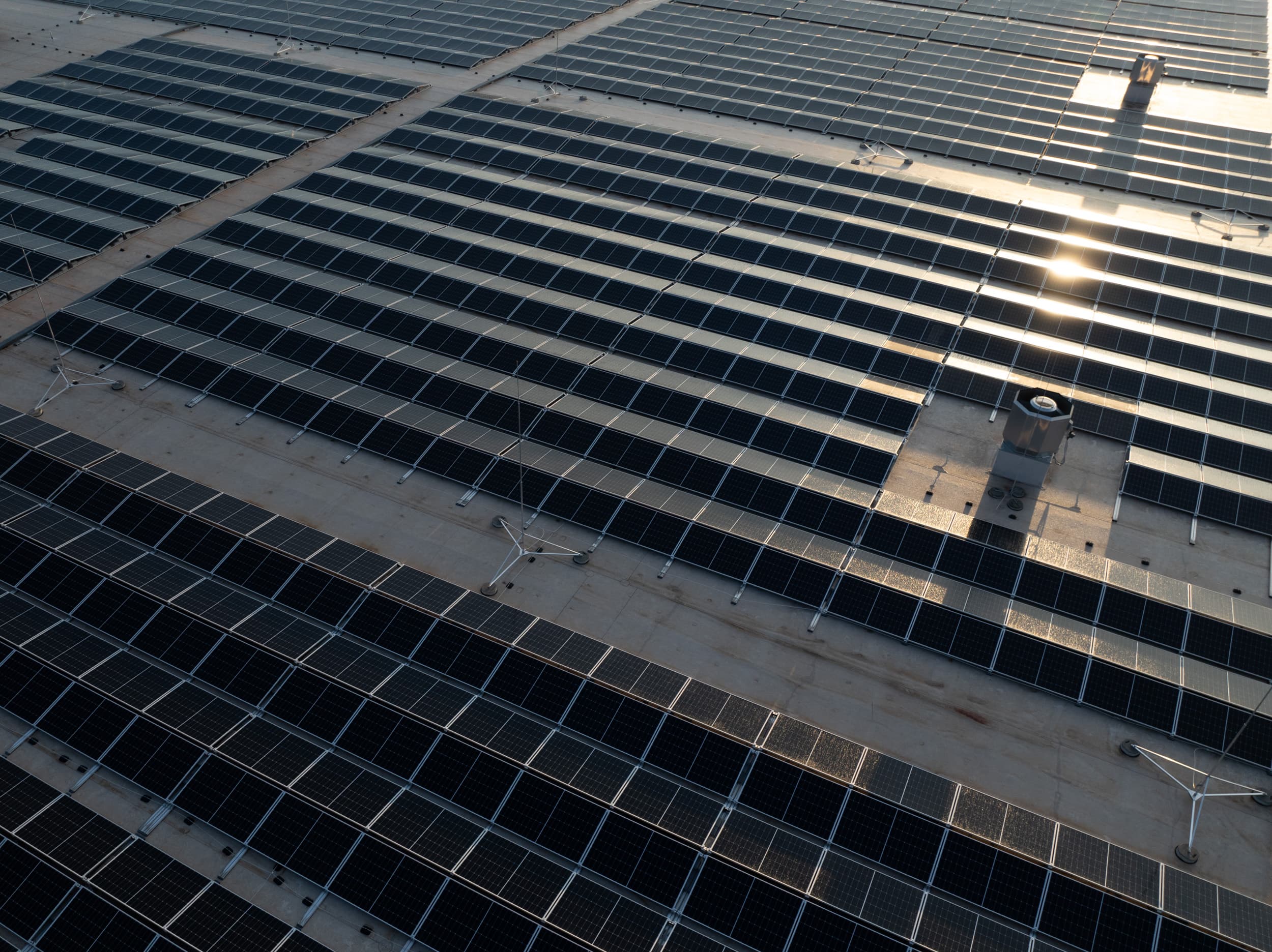 An aerial view of an expansive solar panel array on a flat rooftop, capturing sunlight reflection on several panels.