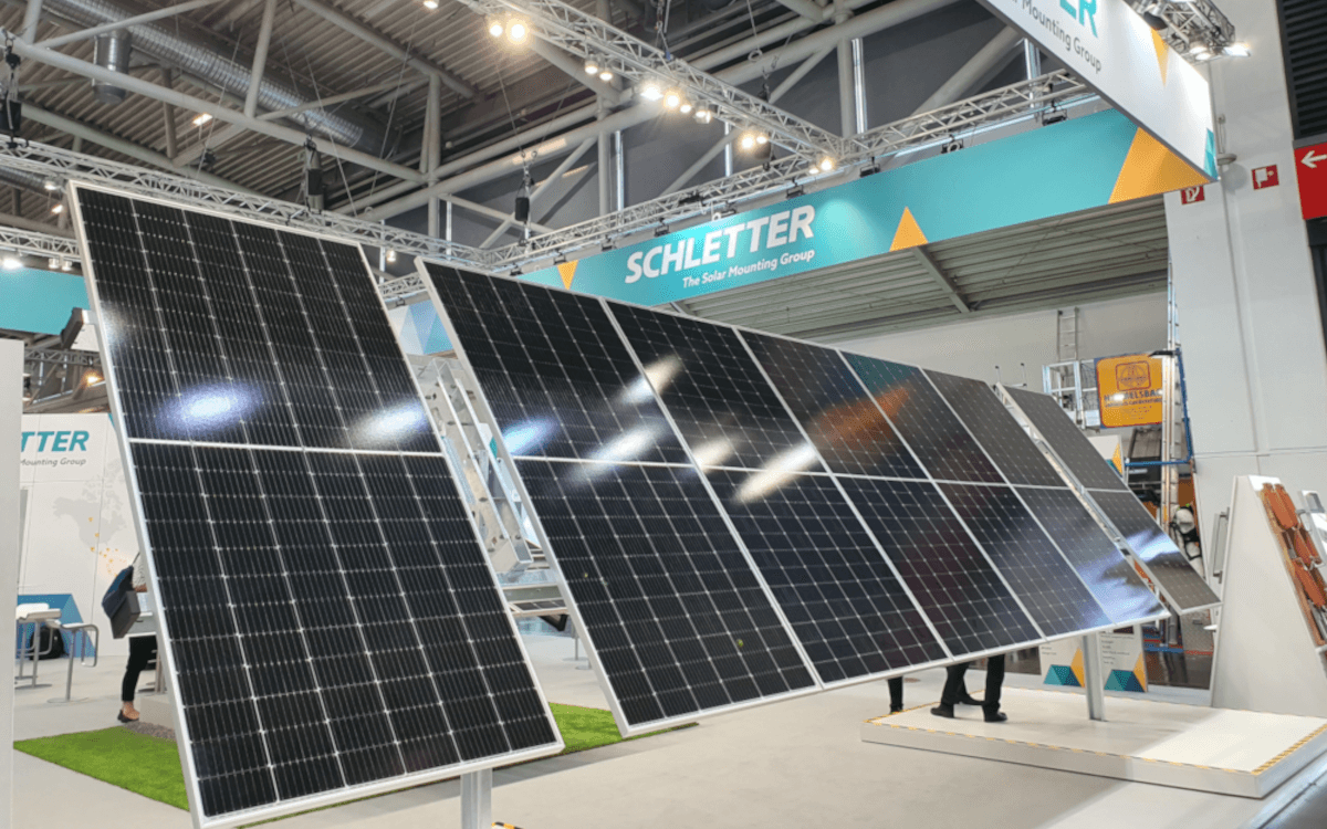 Solar panels displayed at a Schletter booth during an indoor exhibition, with overhead lighting and an industrial ceiling visible.