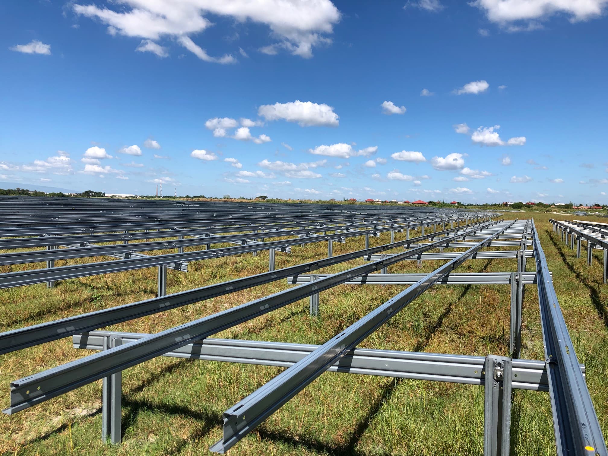 Rows of metallic frames installed on a grassy field under a partly cloudy sky, presumably for solar panel mounting.