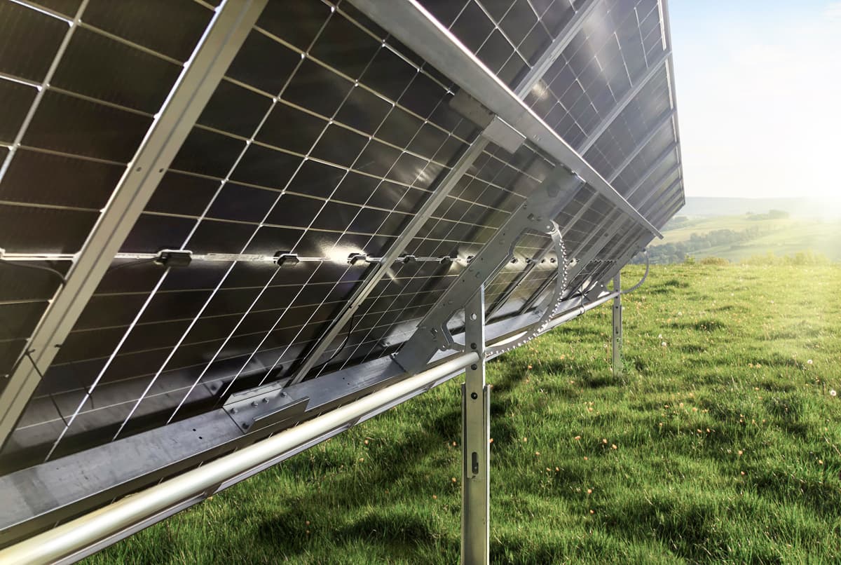 Close-up view of a solar panel array installed on a grassy hillside, with a clear blue sky in the background.