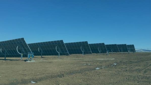 A row of large solar panels installed on a vast, barren land under a clear blue sky.