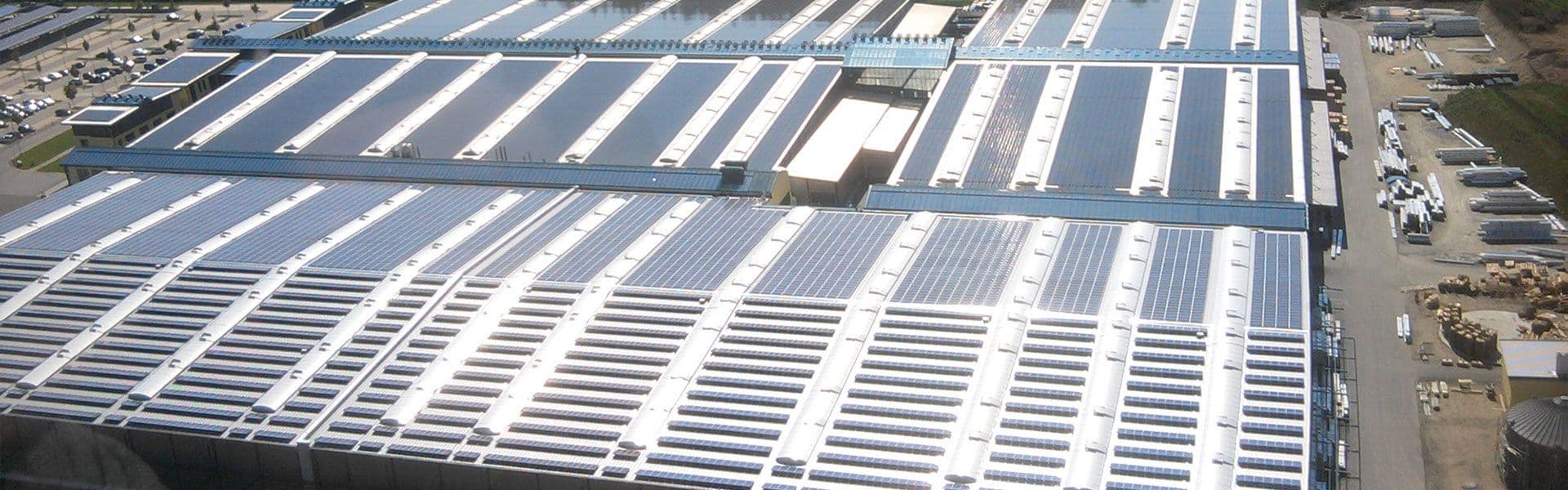 Aerial view of a large industrial facility with multiple buildings, each roof equipped with numerous solar panels.