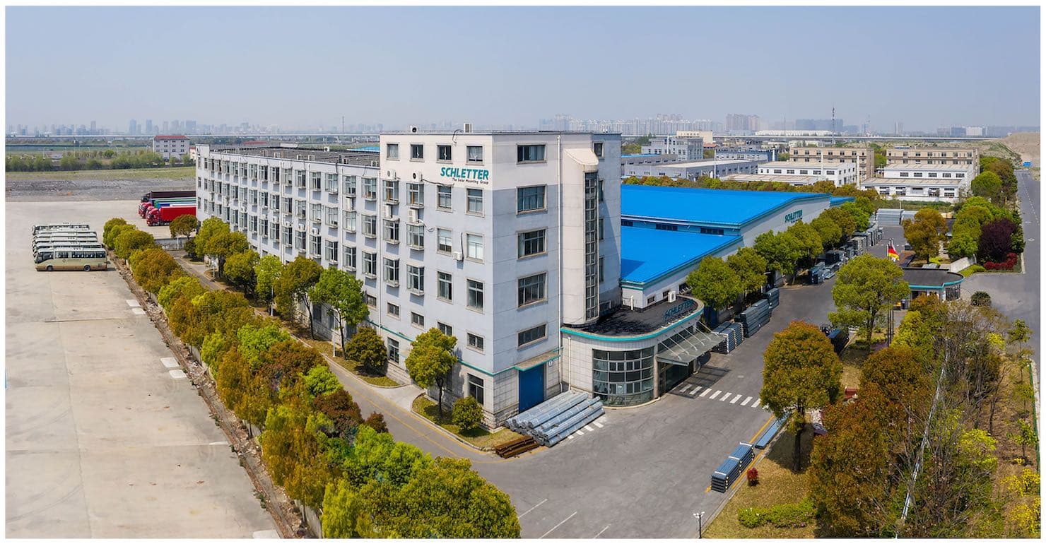 Aerial view of an industrial factory complex featuring multiple buildings, including a large white structure marked "SOLETEK," with blue roofs and surrounded by landscaped areas and parked vehicles.