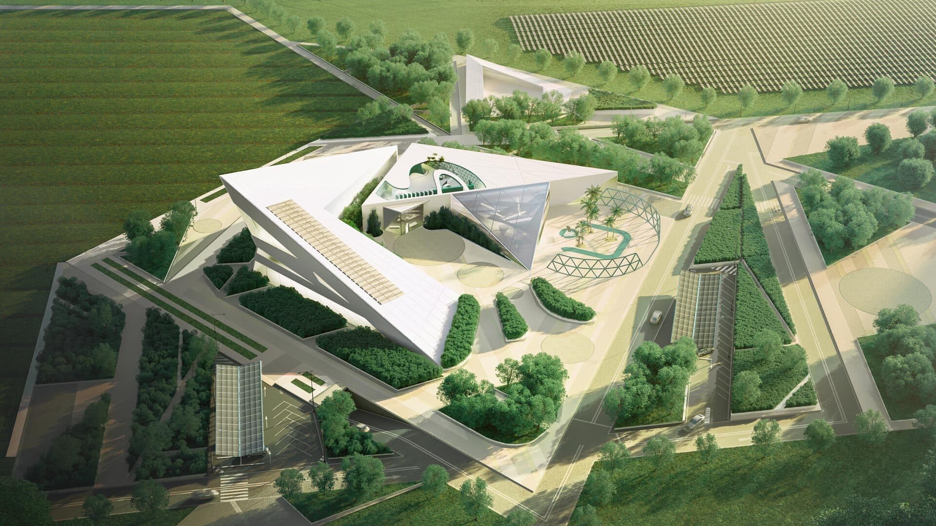 Aerial view of a contemporary, geometric building complex set within green fields, featuring angular structures, landscaped areas, and intersecting roads.