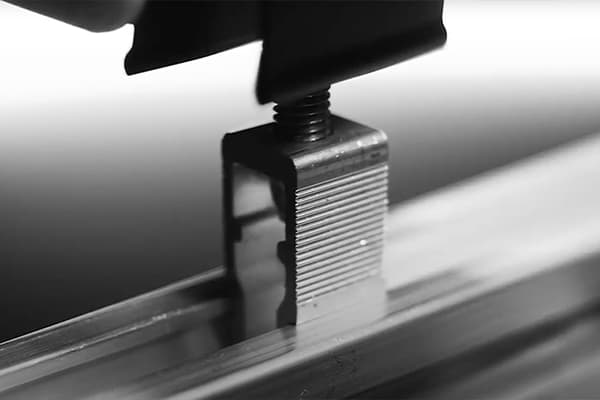 Close-up of a metal clamp tightening a screw on a grooved metallic beam, likely part of an assembly or manufacturing process.