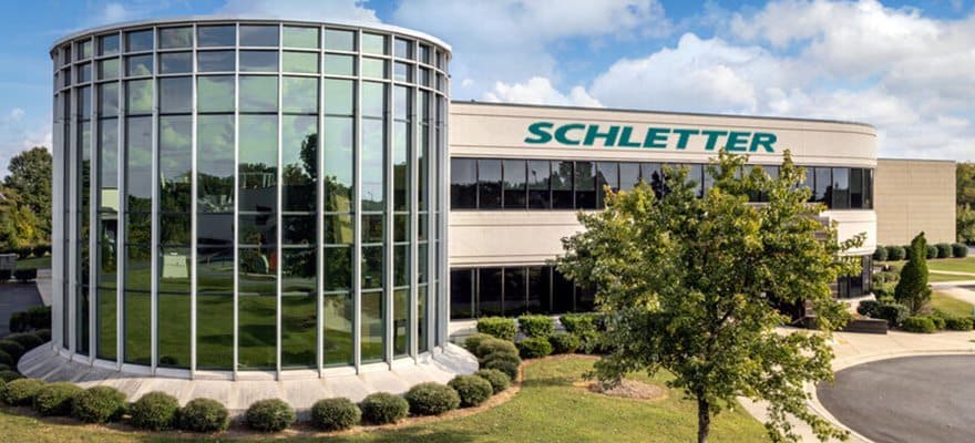 Modern office building with large glass atrium and the name "Schletter" displayed prominently on the front. Surrounding the building are manicured lawns and trees.