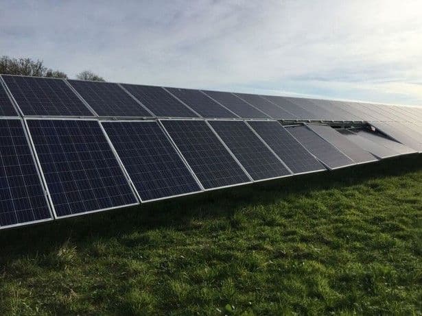 A large array of solar panels is installed in a grassy field under a partly cloudy sky.